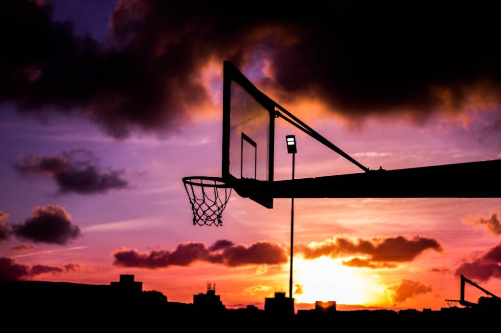 Stunning silhouette of a basketball hoop against a vivid sunset sky with dramatic clouds.